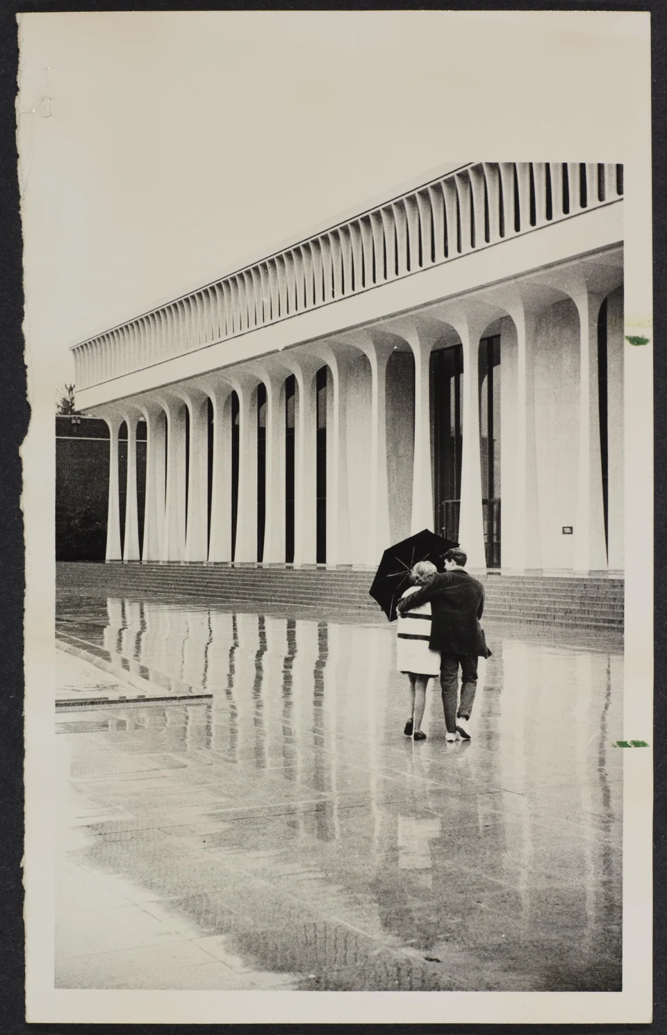 Two people beneath an umbrella outside Robertson Hall, approximately 1960–1970